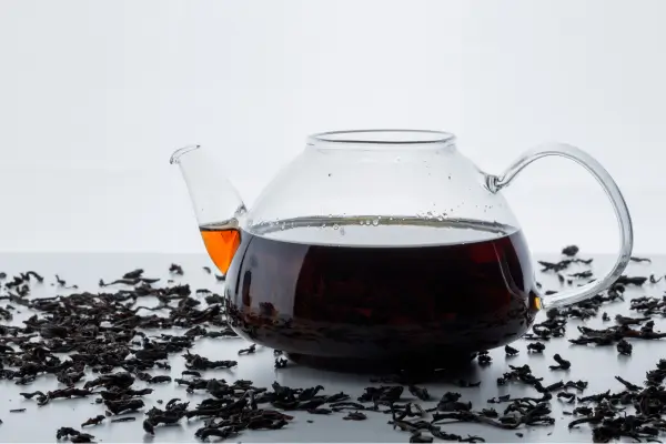 bule em cima da mesa com cja preto e folhas do chá na mesa